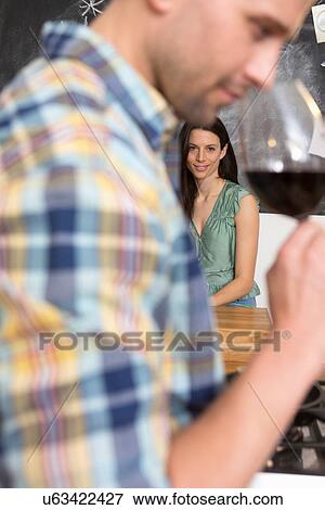 Stock Photo - Mid adult man smelling glass of wine, woman in foreground. Fotosearch