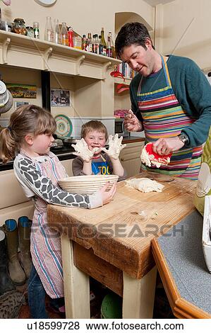 Stock Photo - Mid adult man, son and daughter baking in rustic kitchen. Fotosearch