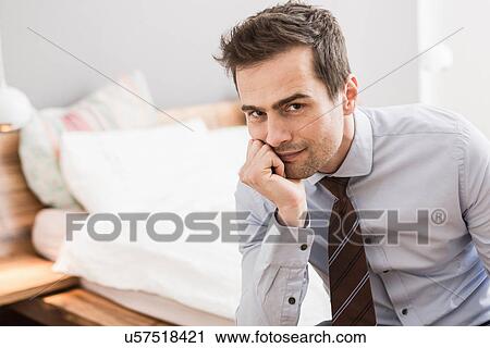 Mid adult man wearing shirt and tie sitting on bed with hand on chin View Large Photo Image Stock Image - Mid adult man wearing shirt and tie sitting on bed with hand on chin. Fotosearch