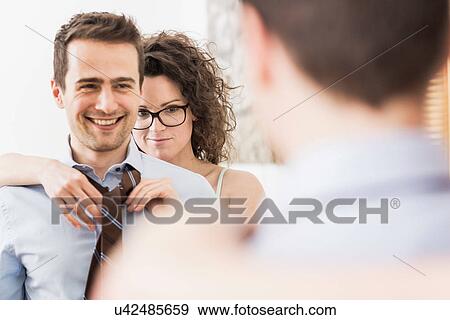 Mid adult woman helping man to fasten tie View Large Photo Image Stock Photo - Mid adult woman helping man to fasten tie. Fotosearch