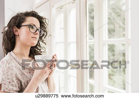 Mid adult woman holding coffee cup, looking out of window View Large Photo Image Stock Photography - Mid adult woman holding coffee cup, looking out of window. Fotosearch