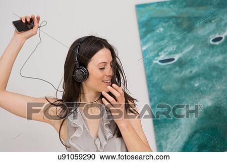 Mid adult woman listening to music through headphones View Large Photo Image Stock Image - Mid adult woman listening to music through headphones. Fotosearch