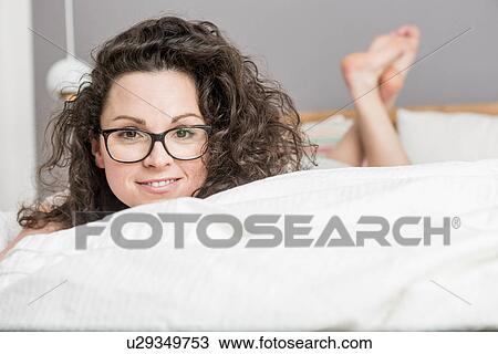 Stock Image - Mid adult woman lying on front on bed. Fotosearch