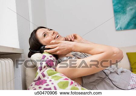 Mid adult woman lying on sofa listening to music through headphones View Large Photo Image Stock Photograph - Mid adult woman lying on sofa listening to music through headphones. Fotosearch