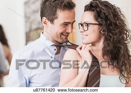 Stock Image - Mid adult woman pulling man's tie. Fotosearch