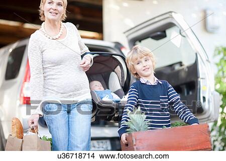 Mother with baby car seat and son carrying box of plants View Large Photo Image Picture - Mother with baby car seat and son carrying box of plants. Fotosearch
