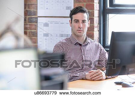Stock Photo - Office worker sitting at desk, portrait. Fotosearch