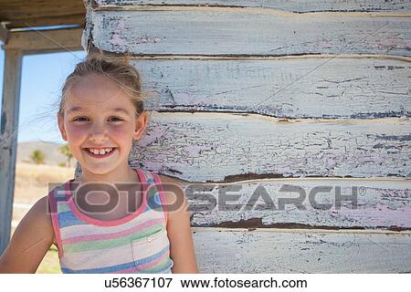 Stock Photo - Portrait of girl wearing striped vest by clapboard cabin. Fotosearch