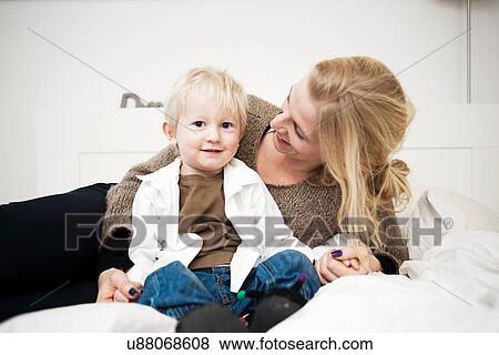 Portrait of mother holding hands with toddler son on bed View Large Photo Image Stock Photo - Portrait of mother holding hands with toddler son on bed. Fotosearch