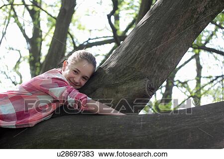 Stock Image - Portrait of young girl lying on top of tree branch. Fotosearch