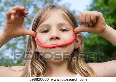 Stock Image - Portrait of young girl making face with liquorice. Fotosearch