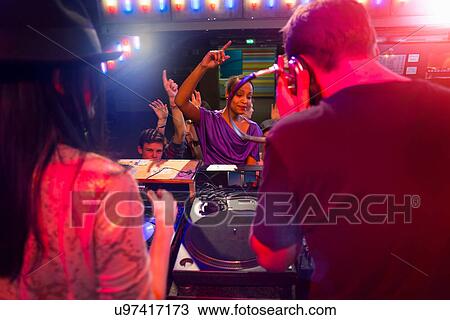 Stock Image - Rear view of disc jockey surrounded by people dancing. Fotosearch