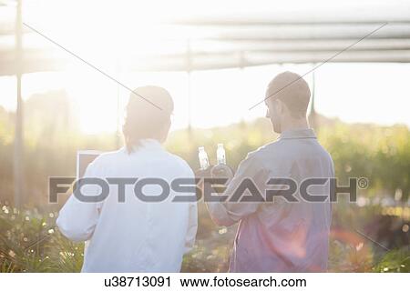 Stock Image - Scientist and worker in plant nursery, looking at bottles. Fotosearch