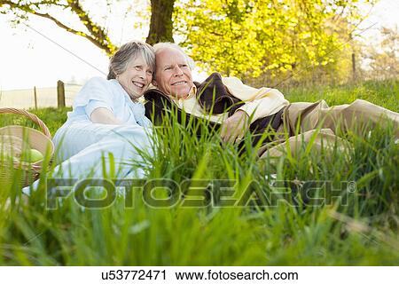 Stock Image - Senior couple relaxing and having picnic on field. Fotosearch