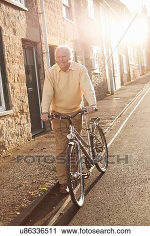 Stock Image - Senior man pushing his bicycle on street. Fotosearch