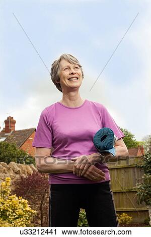 Stock Image - Senior woman carrying yoga mat. Fotosearch