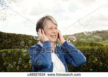 Picture - Senior woman covering ears and laughing at bubbles. Fotosearch