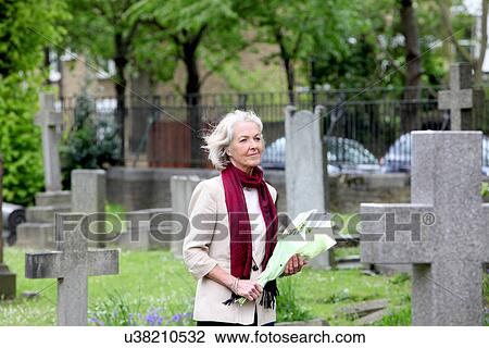 Stock Image - Senior woman holding flowers in graveyard. Fotosearch