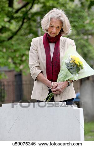 Senior woman holding flowers in graveyard View Large Photo Image Stock Photograph - Senior woman holding flowers in graveyard. Fotosearch