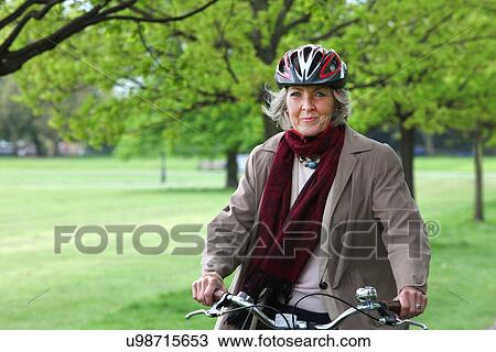 Stock Image - Senior woman riding bicycle in park, portrait. Fotosearch