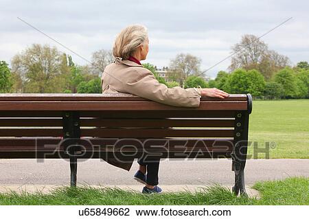 Stock Image - Senior woman sitting on park bench, rear view. Fotosearch