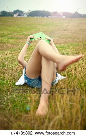Stock Image - Teen girl lying in field, reading book. Fotosearch