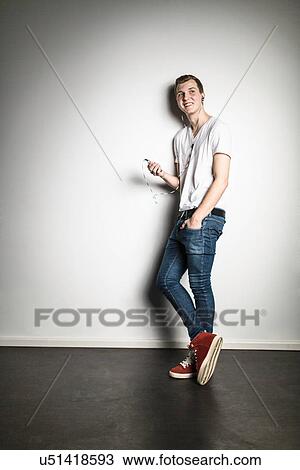 Stock Image - Teenage boy leaning against wall listening to mp3 player. Fotosearch