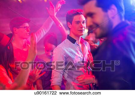 Stock Image - Teenage boy surrounded by group of people dancing at party. Fotosearch