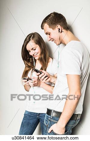Picture - Teenage couple leaning against wall listening to mp3 player. Fotosearch