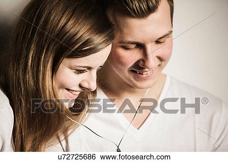 Teenage couple smiling and sharing earphones View Large Photo Image Stock Photograph - Teenage couple smiling and sharing earphones. Fotosearch