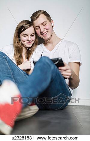 Teenage couple watching digital tablet, sharing earphones View Large Photo Image Stock Image - Teenage couple watching digital tablet, sharing earphones. Fotosearch