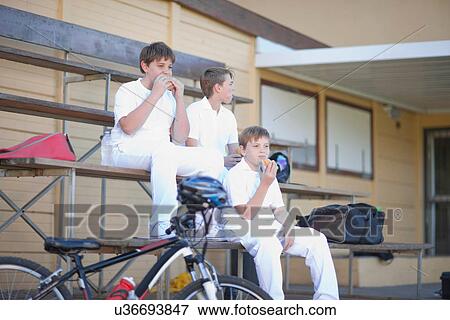 Stock Photo - Three boys sitting on bleachers wearing cricket clothes. Fotosearch
