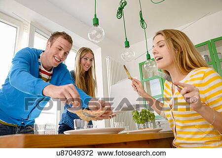 Stock Image - Three young people serving pizza. Fotosearch