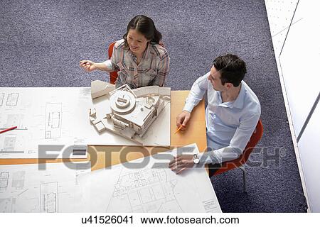 Two architects discussing plans and scale model building in meeting room View Large Photo Image Stock Image - Two architects discussing plans and scale model building in meeting room. Fotosearch