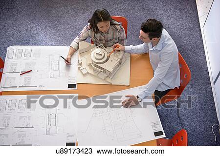 Two architects discussing plans and scale model building in meeting room View Large Photo Image Stock Image - Two architects discussing plans and scale model building in meeting room. Fotosearch