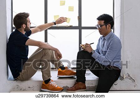 Two young male designers sharing ideas on post it notes View Large Photo Image Picture - Two young male designers sharing ideas on post it notes. Fotosearch