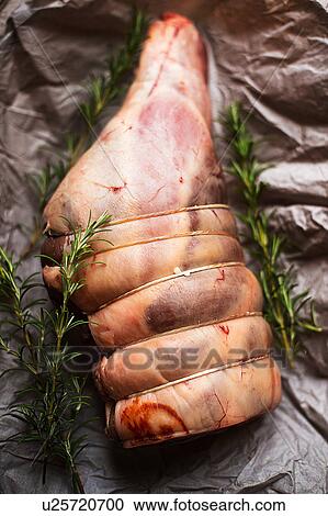 Stock Image - Uncooked leg of lamb with rosemary. Fotosearch