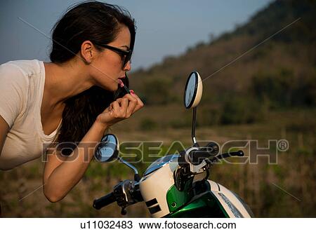 Woman applying lipstick in wing mirror of moped View Large Photo Image Stock Image - Woman applying lipstick in wing mirror of moped. Fotosearch
