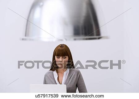 Stock Photo - Woman behind laptop beneath large lampshade. Fotosearch