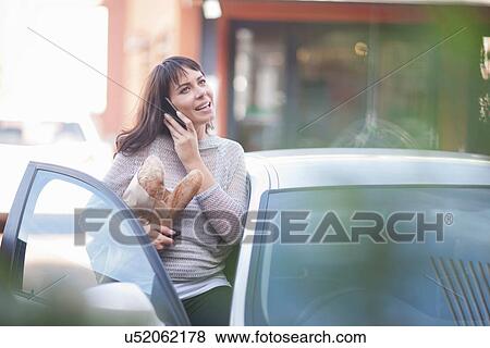 Woman getting in car on cell phone with bread View Large Photo Image Stock Photo - Woman getting in car on cell phone with bread. Fotosearch