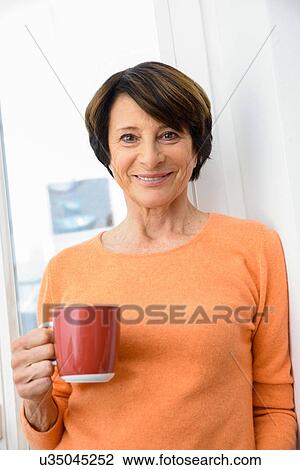 Stock Image - Woman holding mug of coffee, smiling. Fotosearch