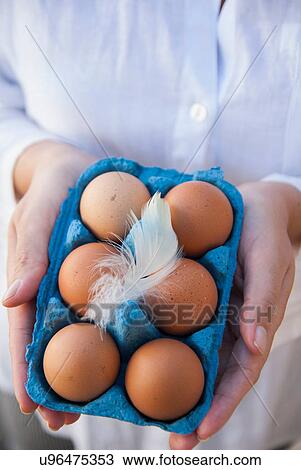 Stock Image - Woman holding six eggs in box with feather. Fotosearch