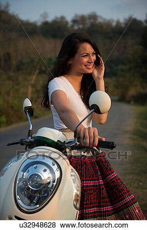 Woman leaning against moped on mobile phone View Large Photo Image Stock Photo - Woman leaning against moped on mobile phone. Fotosearch