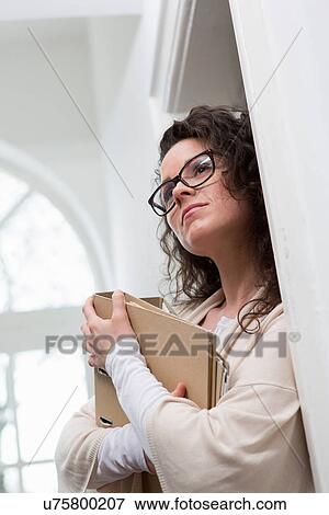 Stock Photo - Woman leaning against wall holding folder. Fotosearch