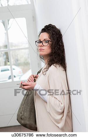 Woman leaning against wall in hallway holding keys and handbag View Large Photo Image Stock Photograph - Woman leaning against wall in hallway holding keys and handbag. Fotosearch