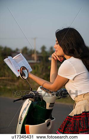 Stock Image - Woman leaning on moped reading book. Fotosearch