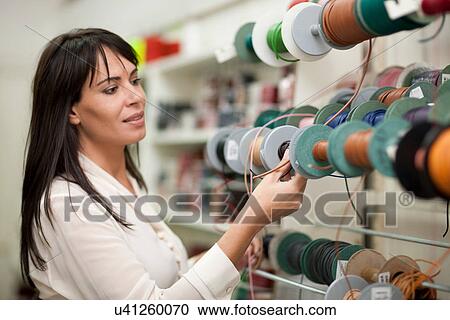 Stock Image - Woman looking at spools of thread in store. Fotosearch