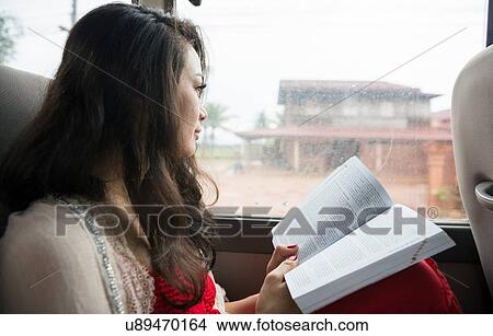 Picture - Woman looking out of window on bus with book. Fotosearch