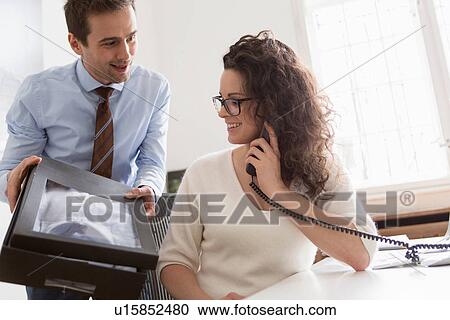 Stock Image - Woman on telephone call, man picking up package of new shirt. Fotosearch