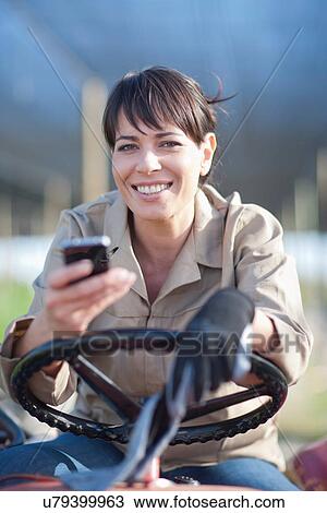 Stock Image - Woman on vehicle with cellphone in plant nursery. Fotosearch